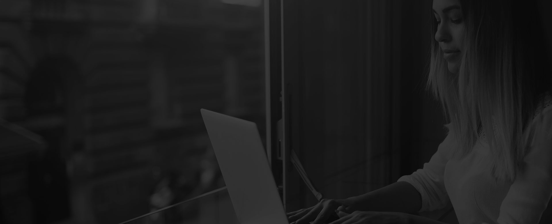 A woman sitting at a window, working on her laptop.